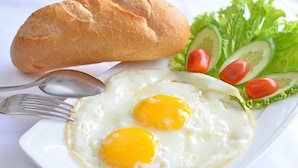 A plate with two sunny-side-up eggs, a baguette, and a side salad with cucumber and cherry tomatoes. - Ngoc Tran Homestay (Ea Kao)