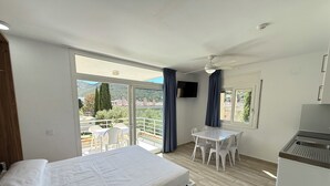 A bedroom with a bed, a small table, a TV, and a balcony with a view.