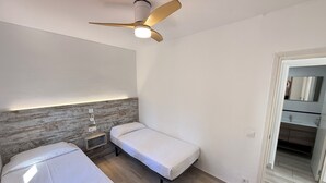 A bedroom with two single beds, a ceiling fan, a bedside table, and a nightstand.