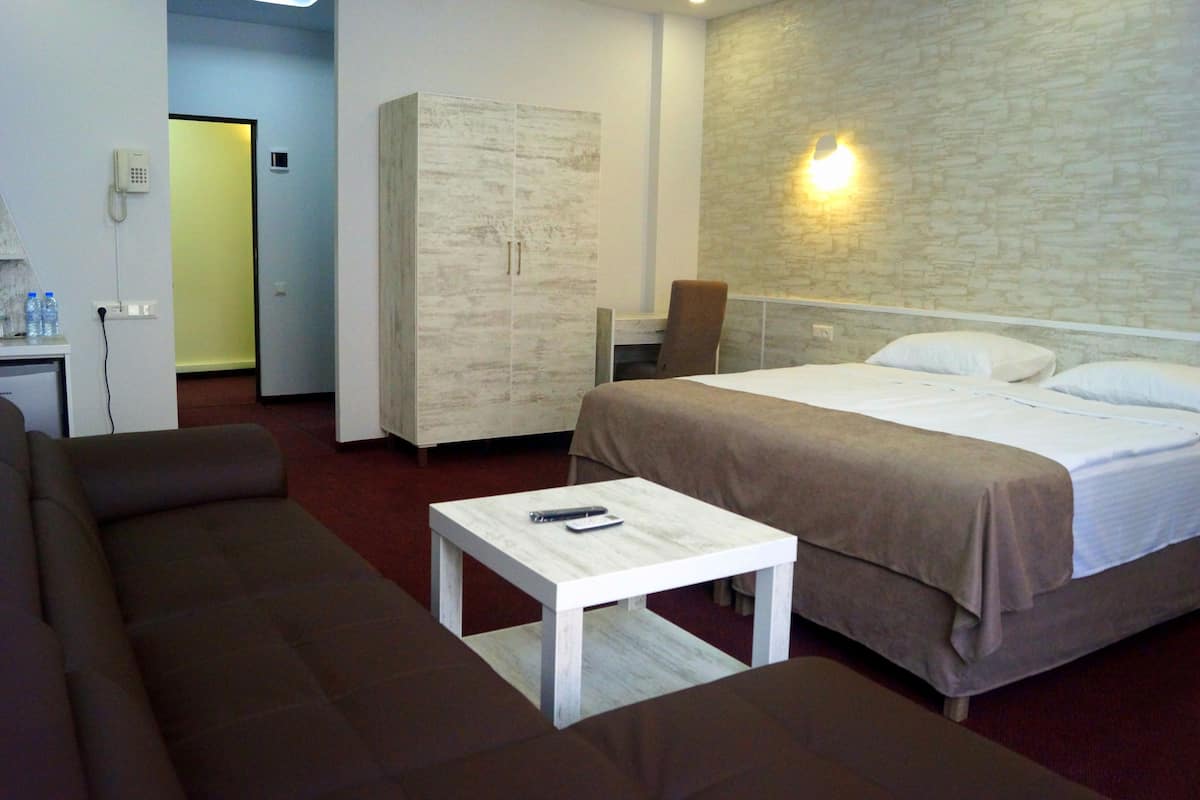 A hotel room with a bed, a sofa, a small table, a wardrobe, and a desk with a chair.