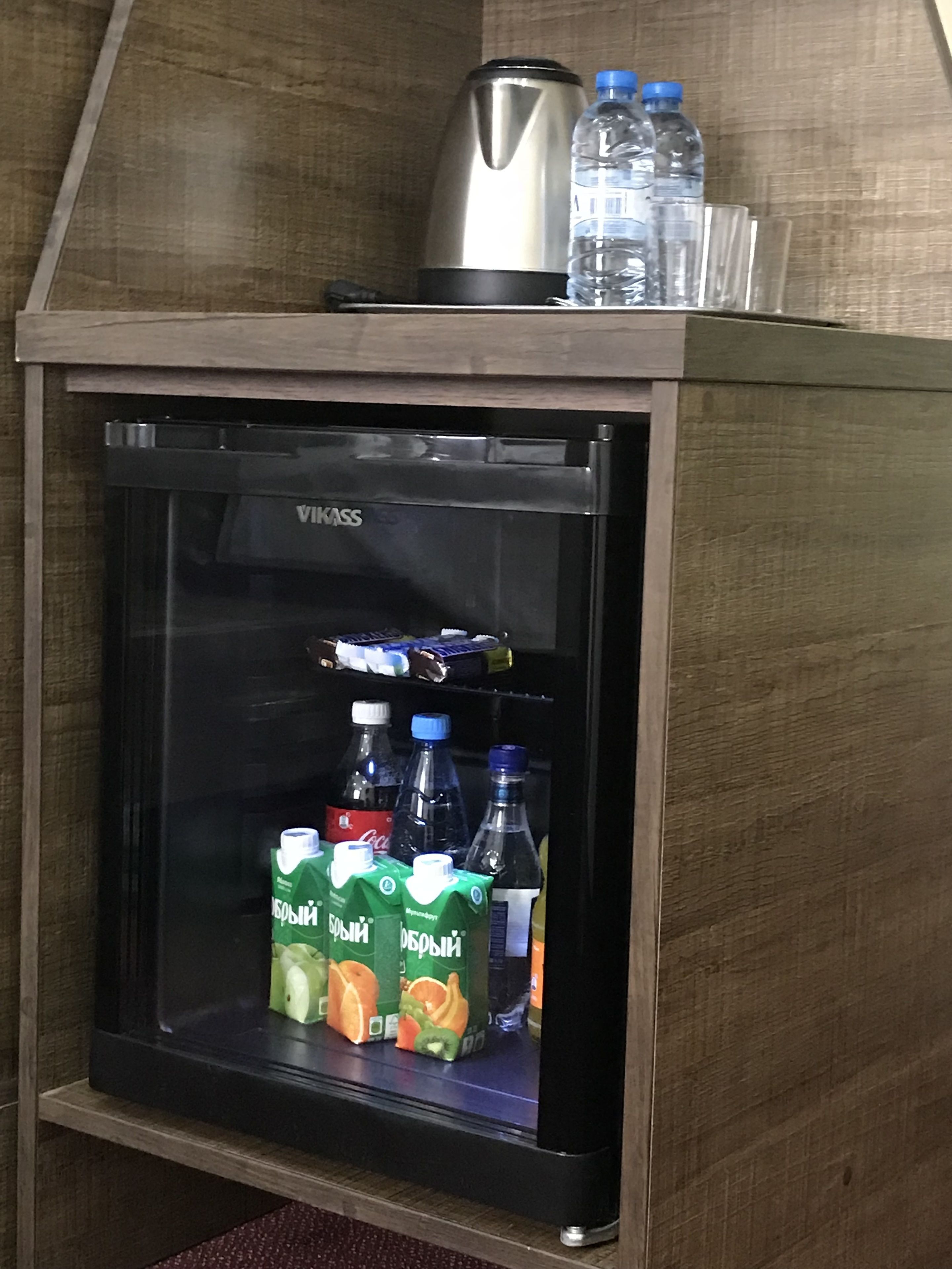 A compact refrigerator with a glass door, containing several bottles and cartons of beverages.