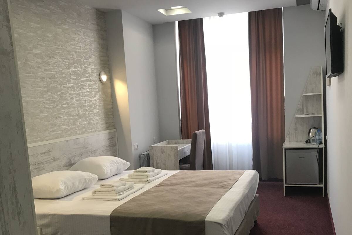 A hotel room with a bed, a desk, a chair, a wardrobe, and a TV.