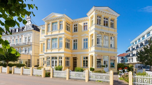 A yellow building with 'AM MEER' signage, a white fence, and a clear blue sky.