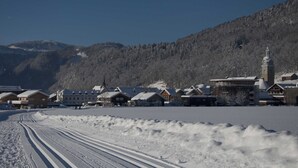 Un pueblo cubierto de nieve con casas de madera tradicionales, una iglesia y montañas al fondo.