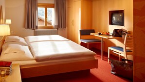 Una habitación de hotel con una cama, un escritorio con silla, un televisor y una ventana con cortinas.