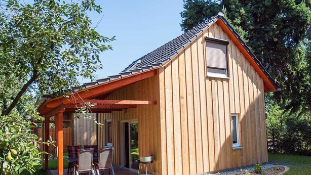 Una cabaña de madera con un porche cubierto y un pequeño espacio exterior con mobiliario.