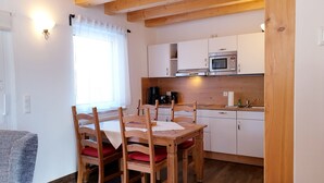 Una cocina acogedora con armarios de madera, una mesa de comedor con sillas y una ventana con cortinas traslúcidas.