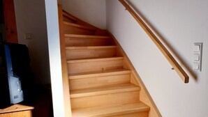 Una escalera de madera con barandilla, un interruptor de pared y un mueble de madera con un televisor.