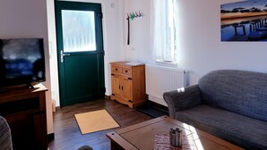 Una sala de estar con televisor, una puerta verde, un mueble de madera, un radiador y un sofá.