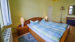 A bedroom with a wooden bed, two bedside lamps, a nightstand, a radiator, a blue rug, and a hanging light fixture.
