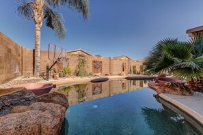 A swimming pool with a basketball hoop, palm trees, and a brick wall.