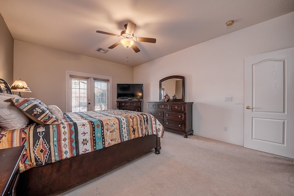 A bedroom with a bed, dresser, mirror, ceiling fan, and a TV.