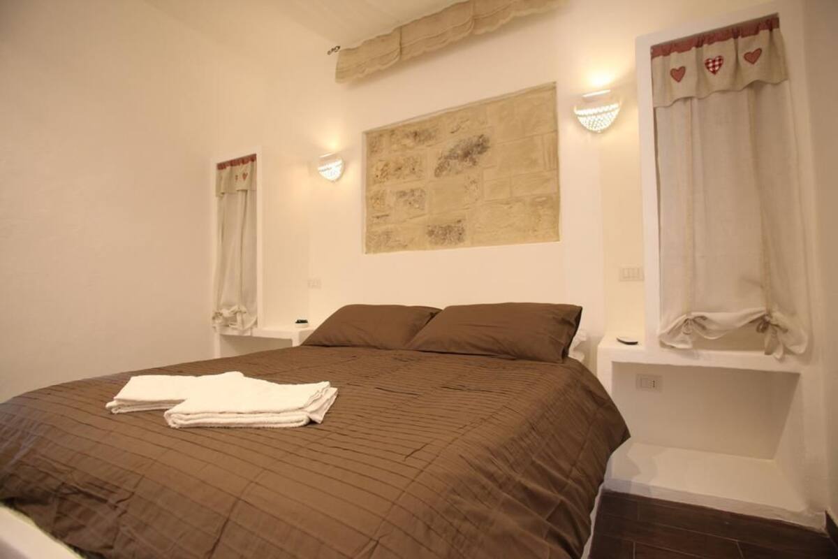 A bedroom with a large bed, two bedside tables, a wall-mounted light, and a decorative wall piece.