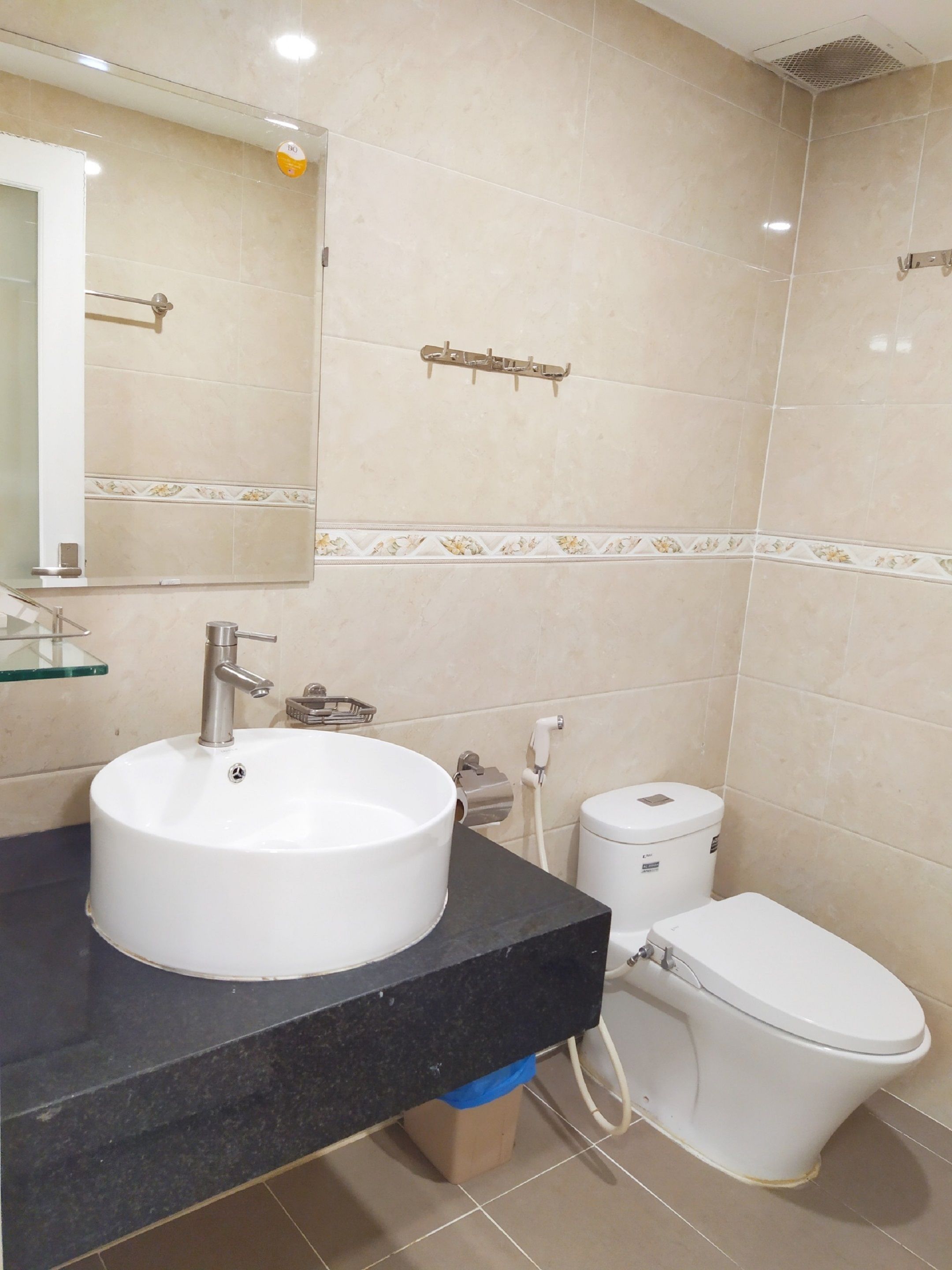 A bathroom with a round white sink, a mirror, a toilet, and a towel rack.