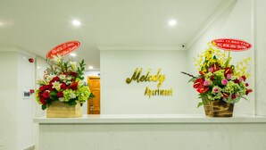 A reception desk with a sign reading "Melody Apartment" and two flower arrangements.