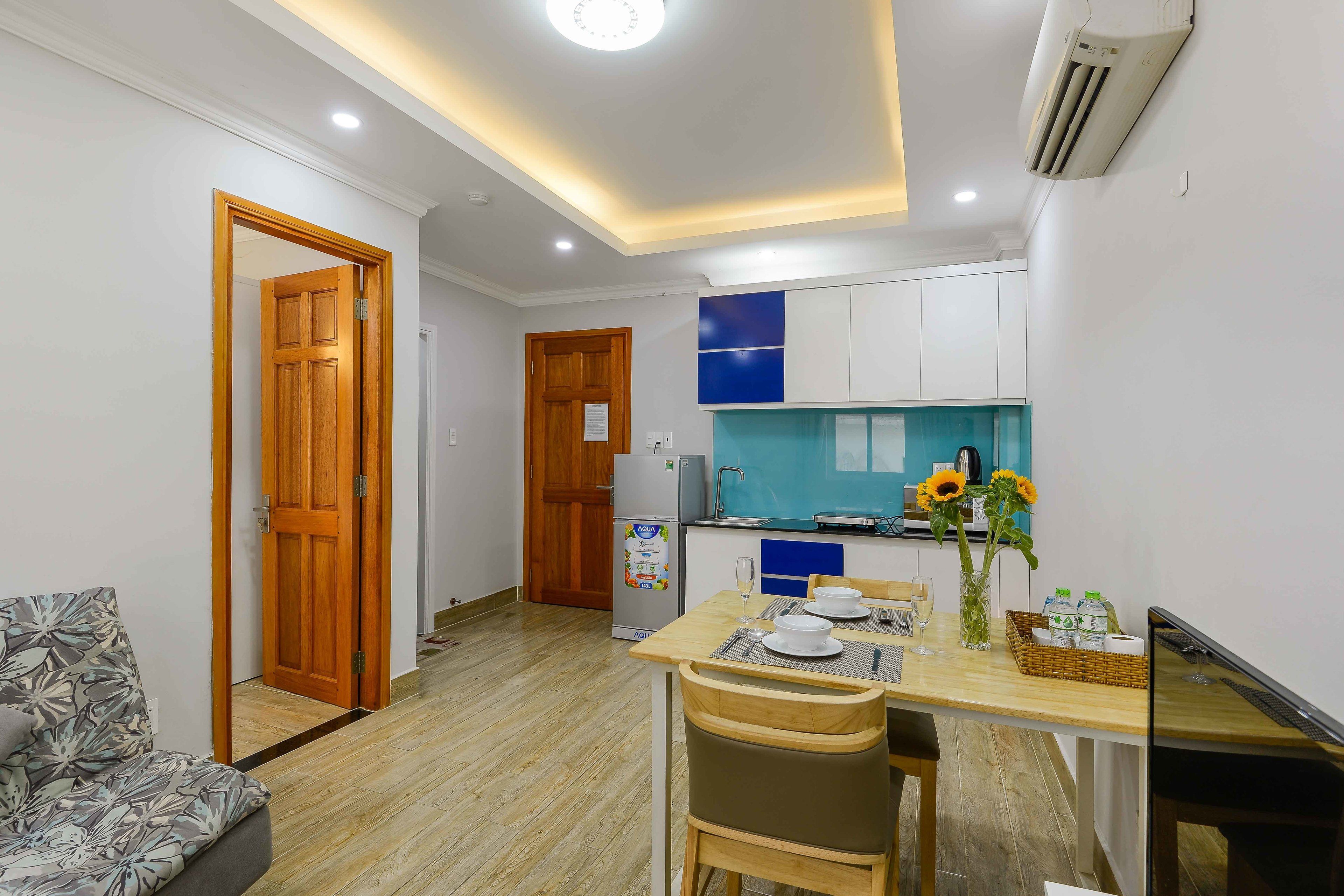 A compact kitchen with a refrigerator, sink, and a blue backsplash. There is a dining table with chairs and a vase with flowers.