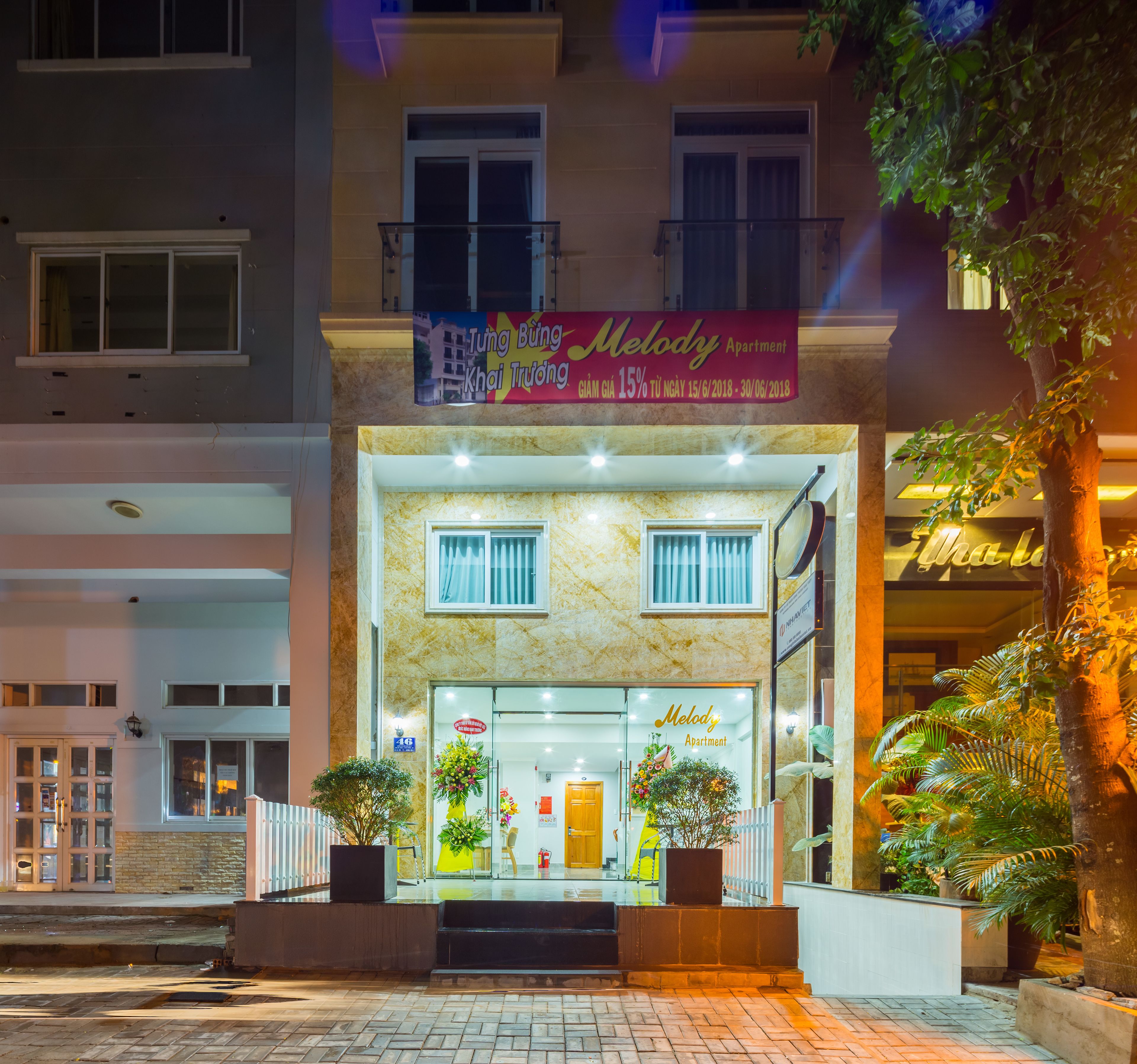 A two-story building with a sign for 'Melody Apartment' and a promotional banner above the entrance.