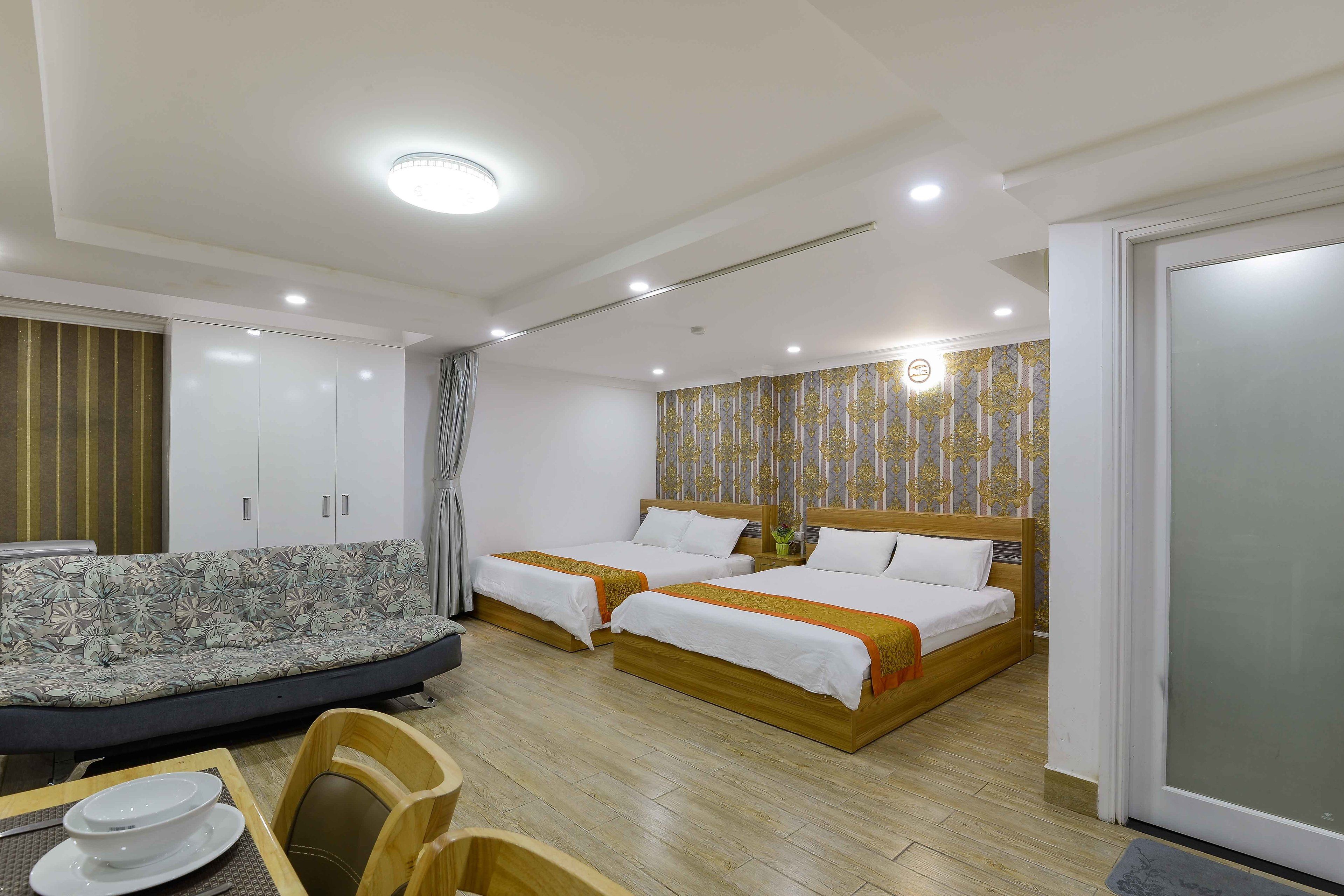 A hotel room with two single beds, a sofa, a dining table with chairs, and a wardrobe.