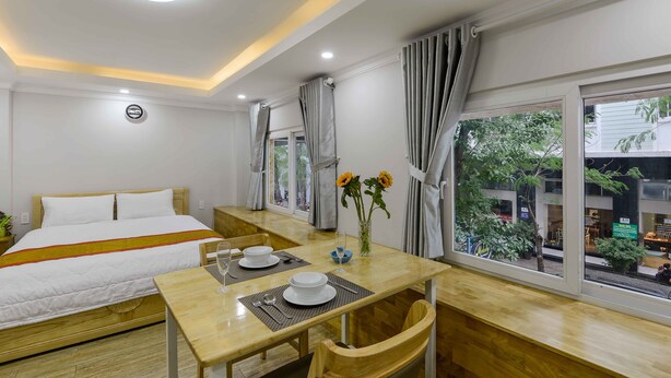 A hotel room with a bed, a dining table with chairs, a vase with flowers, and a window with curtains.