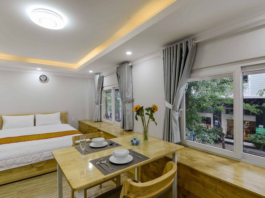 Una habitación de hotel con cama, una mesa de comedor con sillas, un florero con flores y una ventana con cortinas.