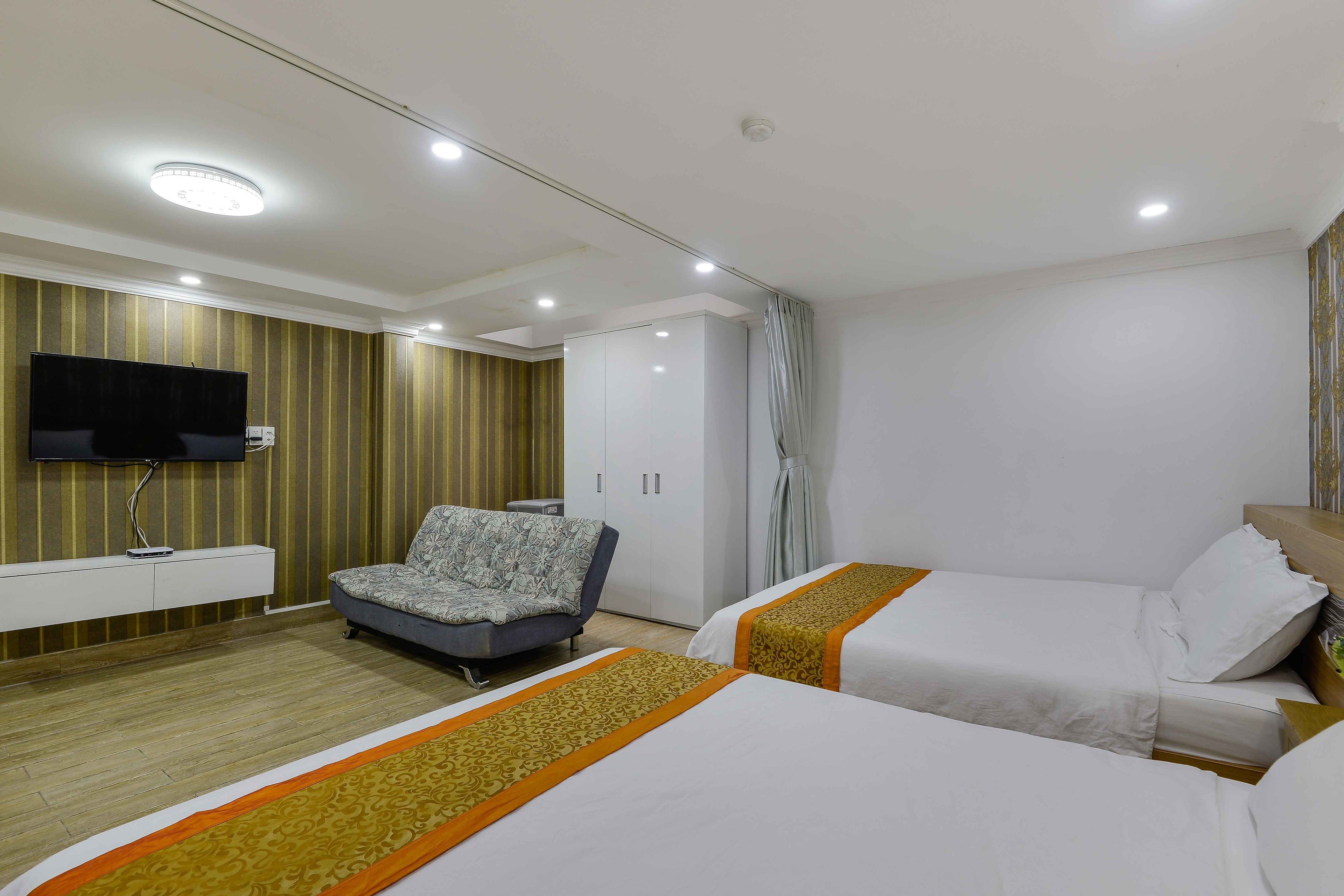 A hotel room with two beds, a sofa, a TV, and a wardrobe.