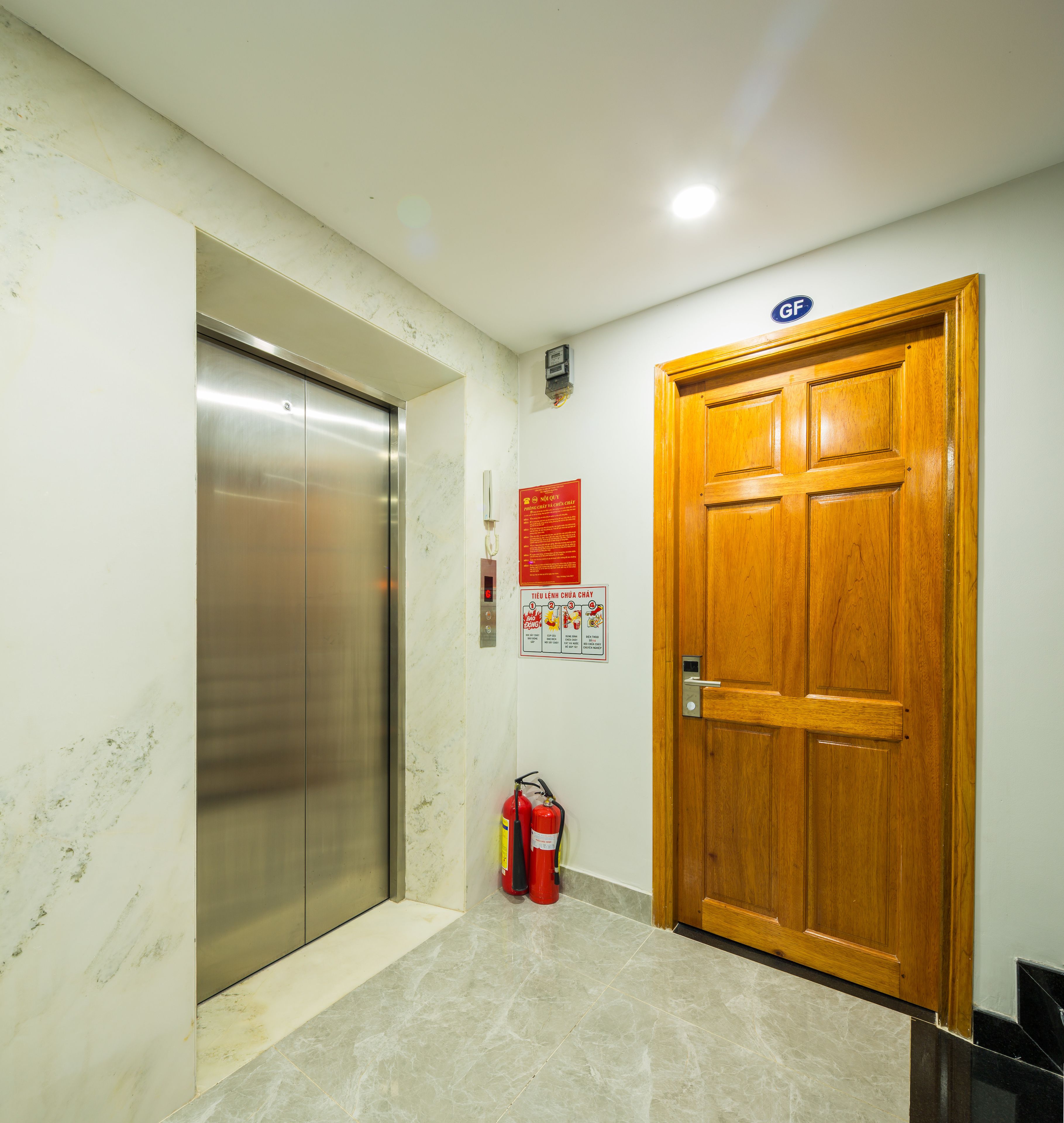 A hallway with a wooden door, a fire extinguisher, and an elevator.