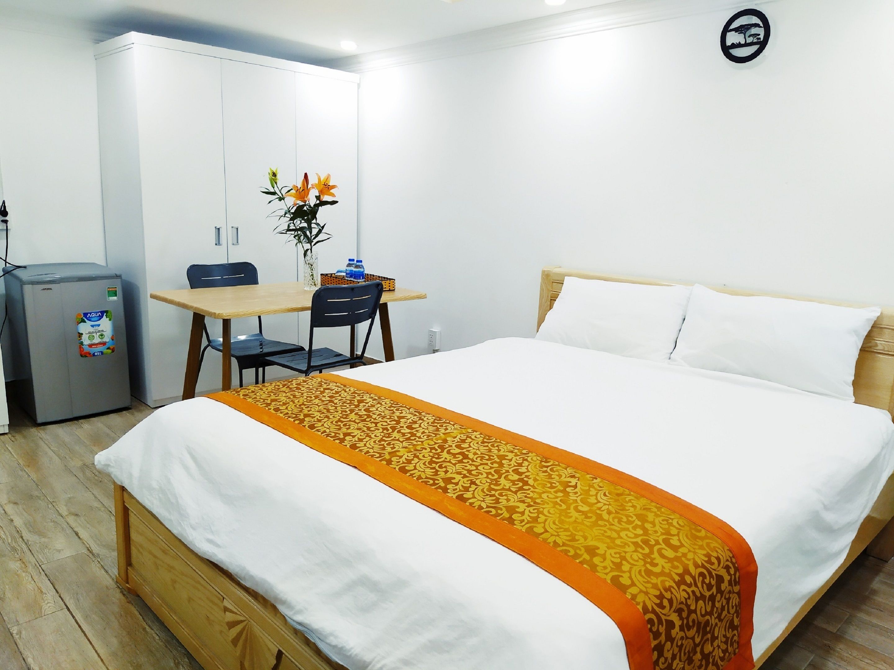 Une chambre d’hôtel équipée d’un lit, d’un bureau, d’une chaise, d’un réfrigérateur et d’un vase avec des fleurs.