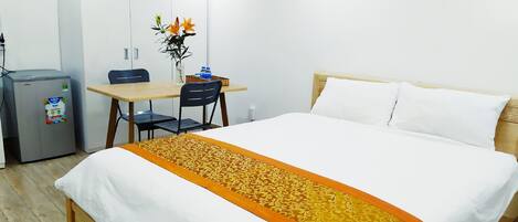 Une chambre d’hôtel équipée d’un lit, d’un bureau, d’une chaise, d’un réfrigérateur et d’un vase avec des fleurs.