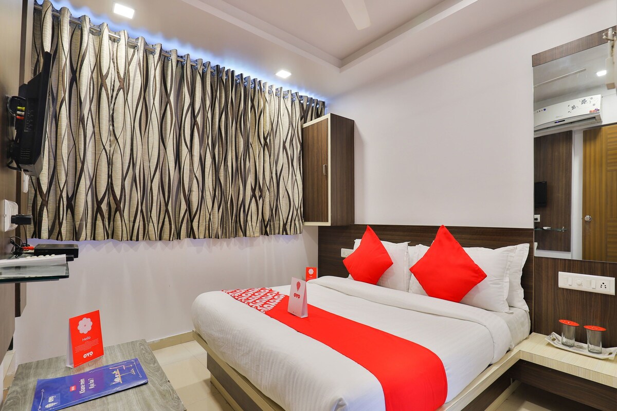 A hotel room with a bed, a bedside table, a mirror, and a curtain with a wavy pattern.