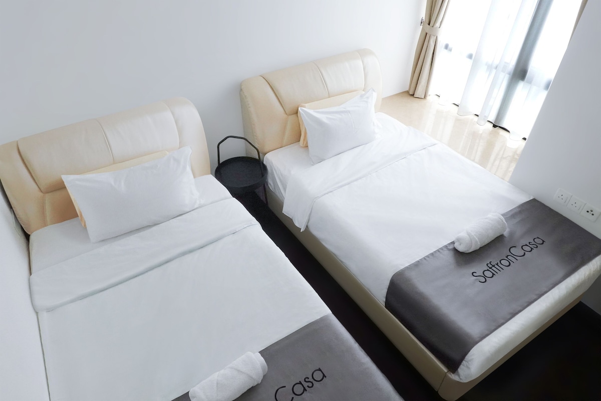 Dos camas con cabeceras, ropa de cama blanca y una manta gris con el texto "SaffronCasa".