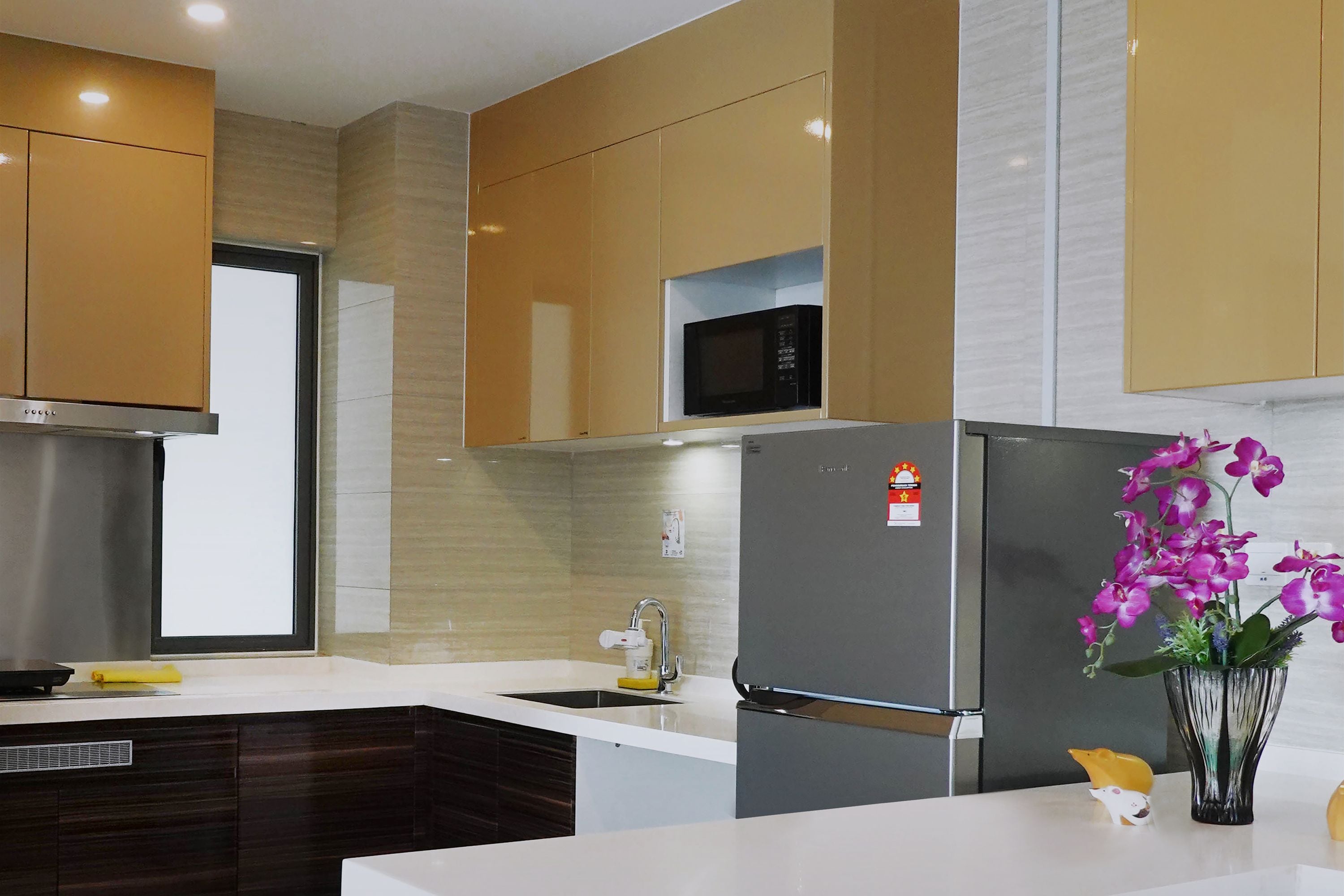 Cozinha moderna com micro-ondas embutido, eletrodomésticos em aço inoxidável e um vaso decorativo com orquídeas.