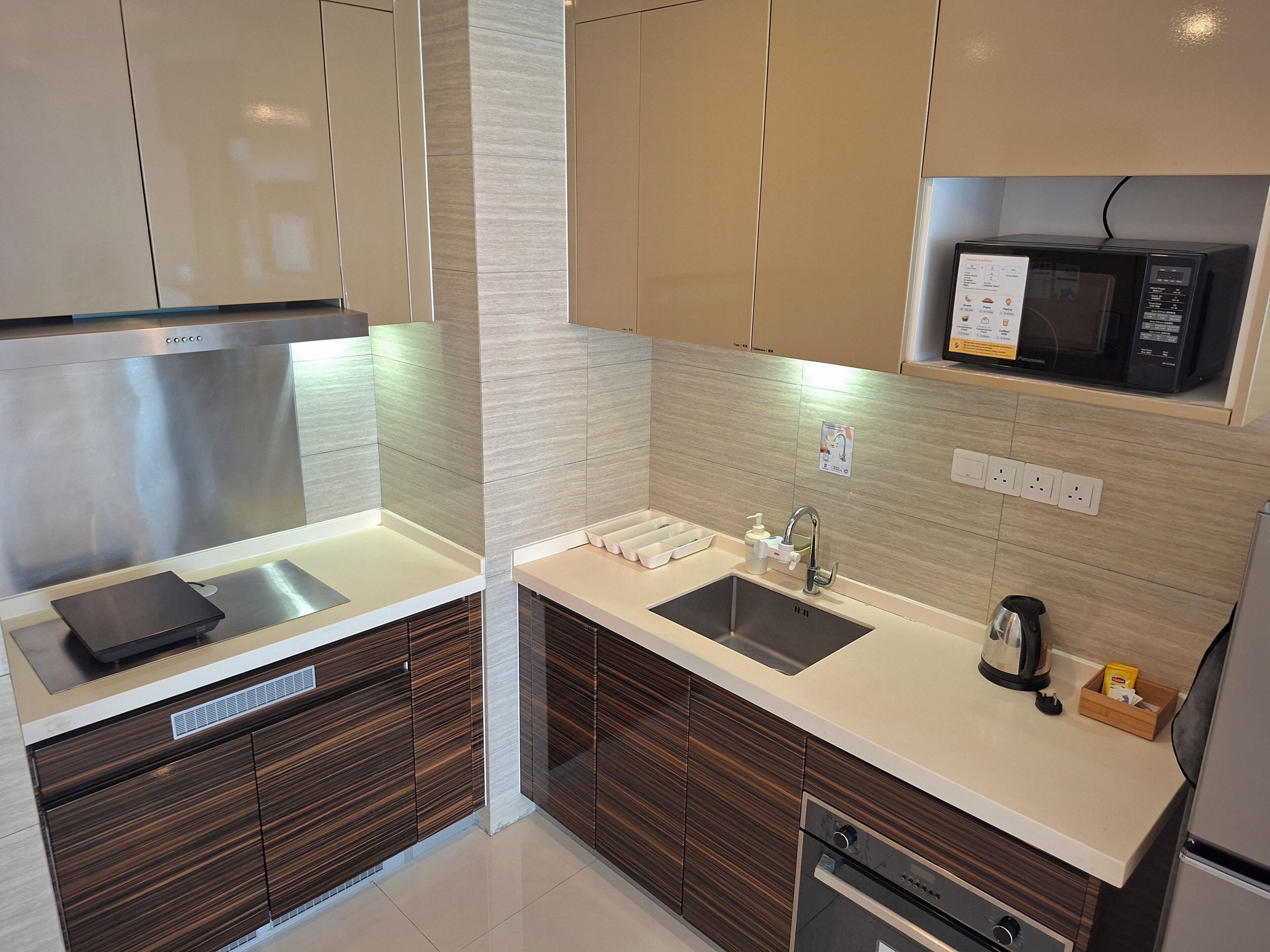 A modern kitchen with a stainless steel range hood, a microwave, a sink with a faucet, and a kettle.