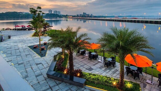A waterfront patio with outdoor seating, palm trees, and a view of the city skyline. - R&F Princess Cove JB By SaffronCasa JB (Johor Bahru)