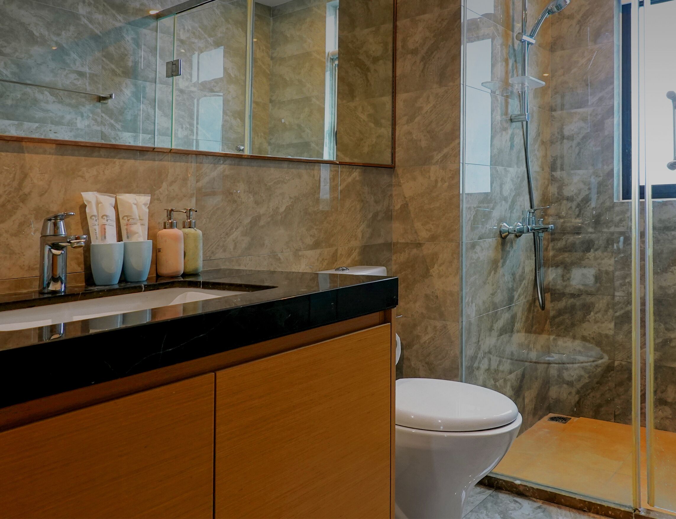A modern bathroom with a marble sink, a glass shower enclosure, and a toilet.