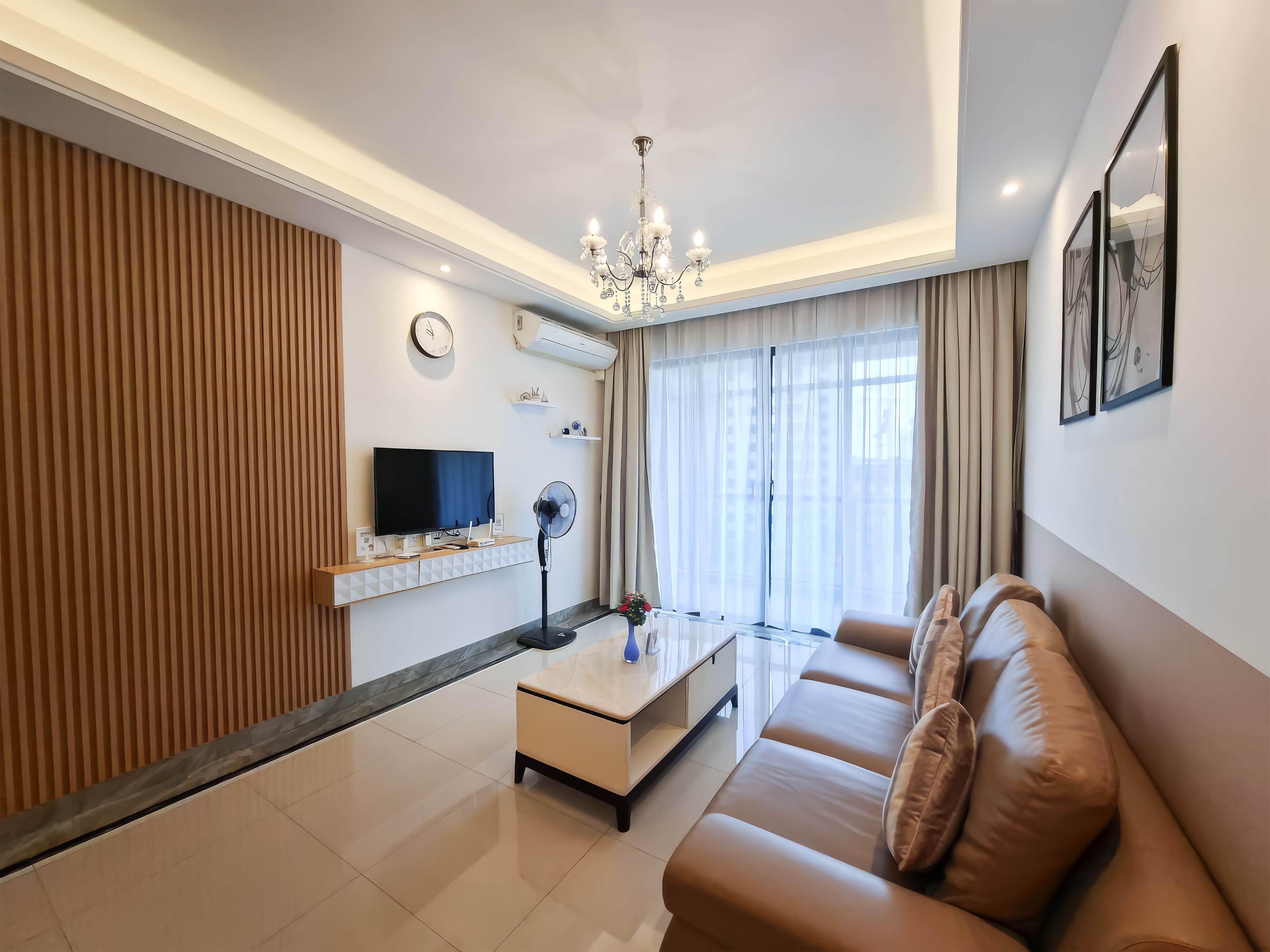 Een moderne woonkamer met een flatscreen televisie, een verticale ventilator, een bank en een kroonluchter.