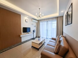 A modern living room with a flat-screen TV, a standing fan, a sofa, and a chandelier.