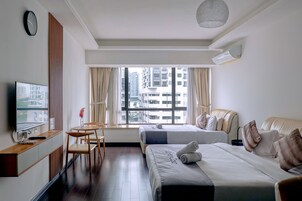 A hotel room with two beds, a TV, a desk, and a window with a city view.