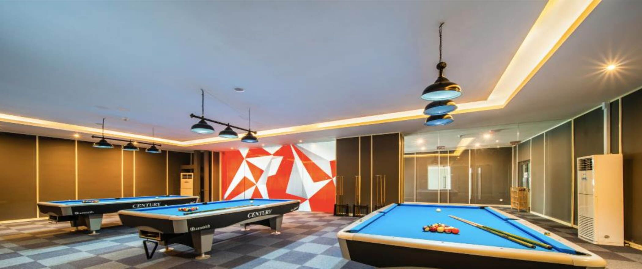 A pool room with two pool tables, overhead lighting, and a geometric wall design.