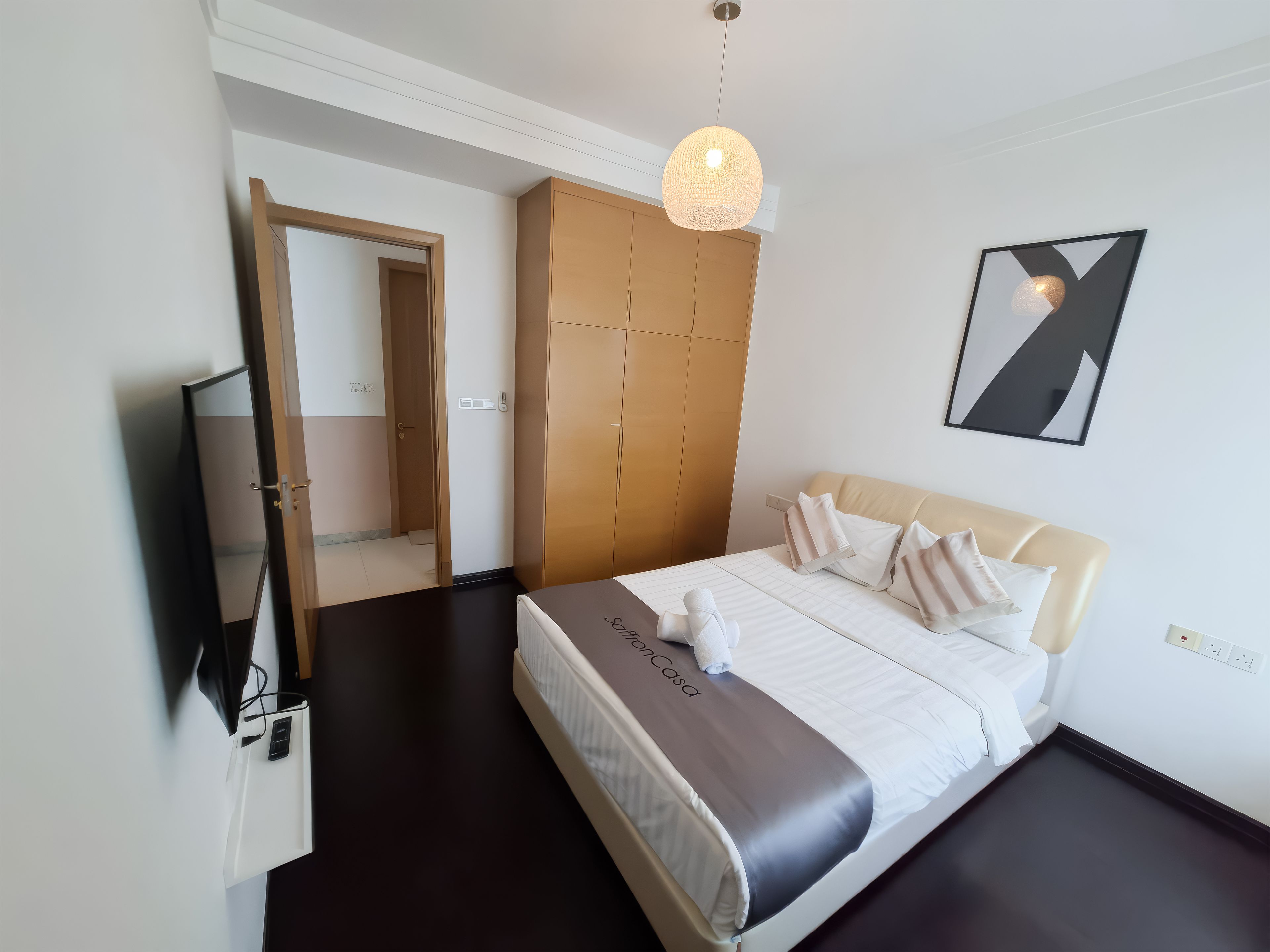A hotel room with a bed, a wardrobe, a mirror, a television, and a pendant light.