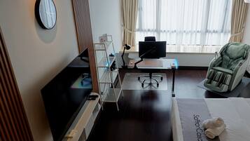 A hotel room with a bed, a desk with a computer, a massage chair, a TV, and a wall clock.