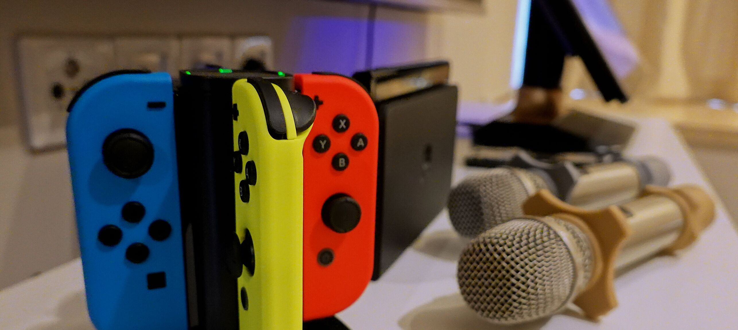 A close-up of four colorful game controllers and a microphone on a table.