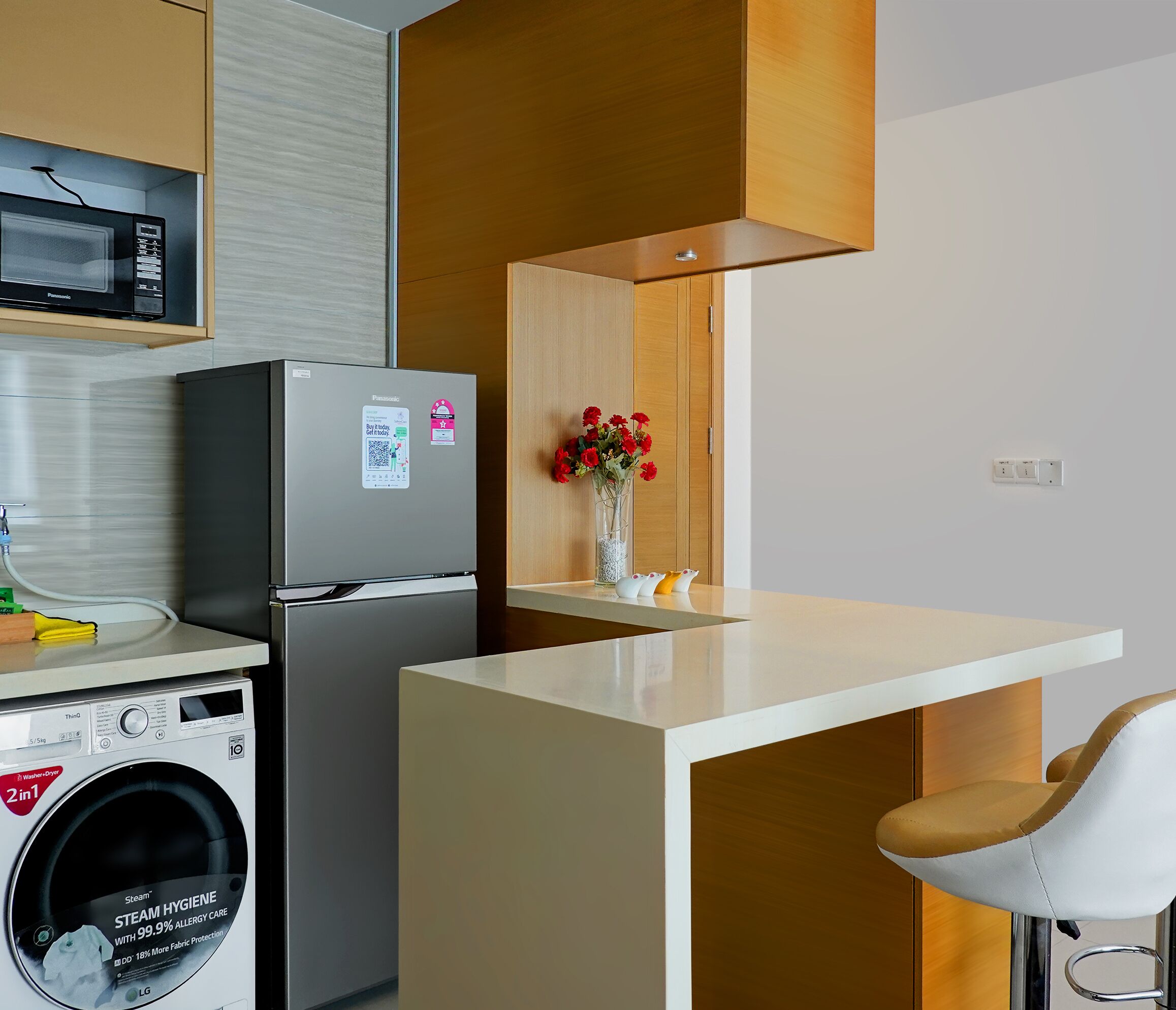 A compact kitchen with a washing machine, a refrigerator, a microwave, and a small dining area with a chair.
