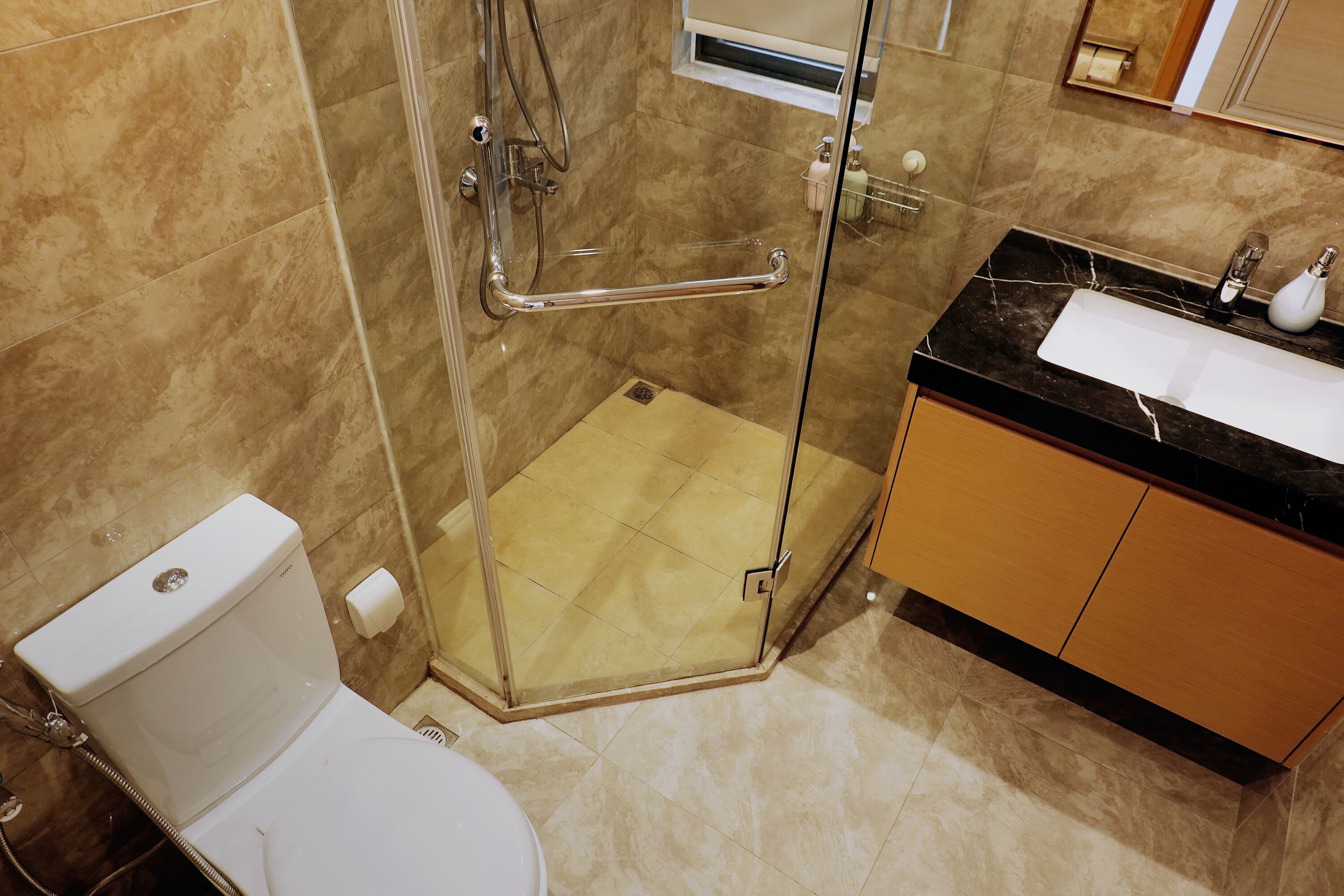 Un baño con ducha envuelta en vidrio, inodoro blanco y lavabo con encimera negra.