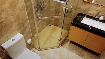 Un baño con ducha envuelta en vidrio, inodoro blanco y lavabo con encimera negra.