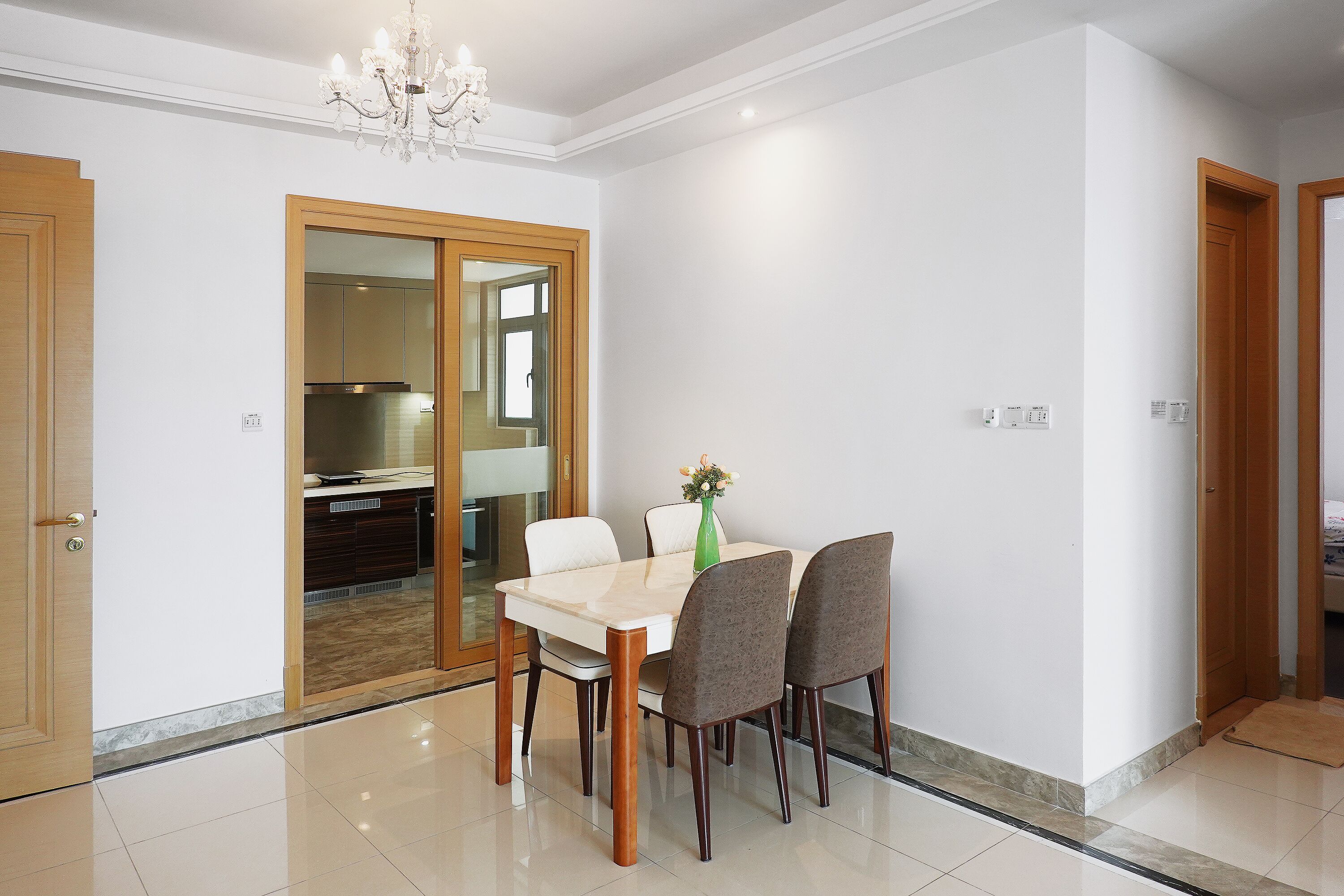 A dining area with a table and chairs, a chandelier, and a sliding glass door leading to a kitchen.