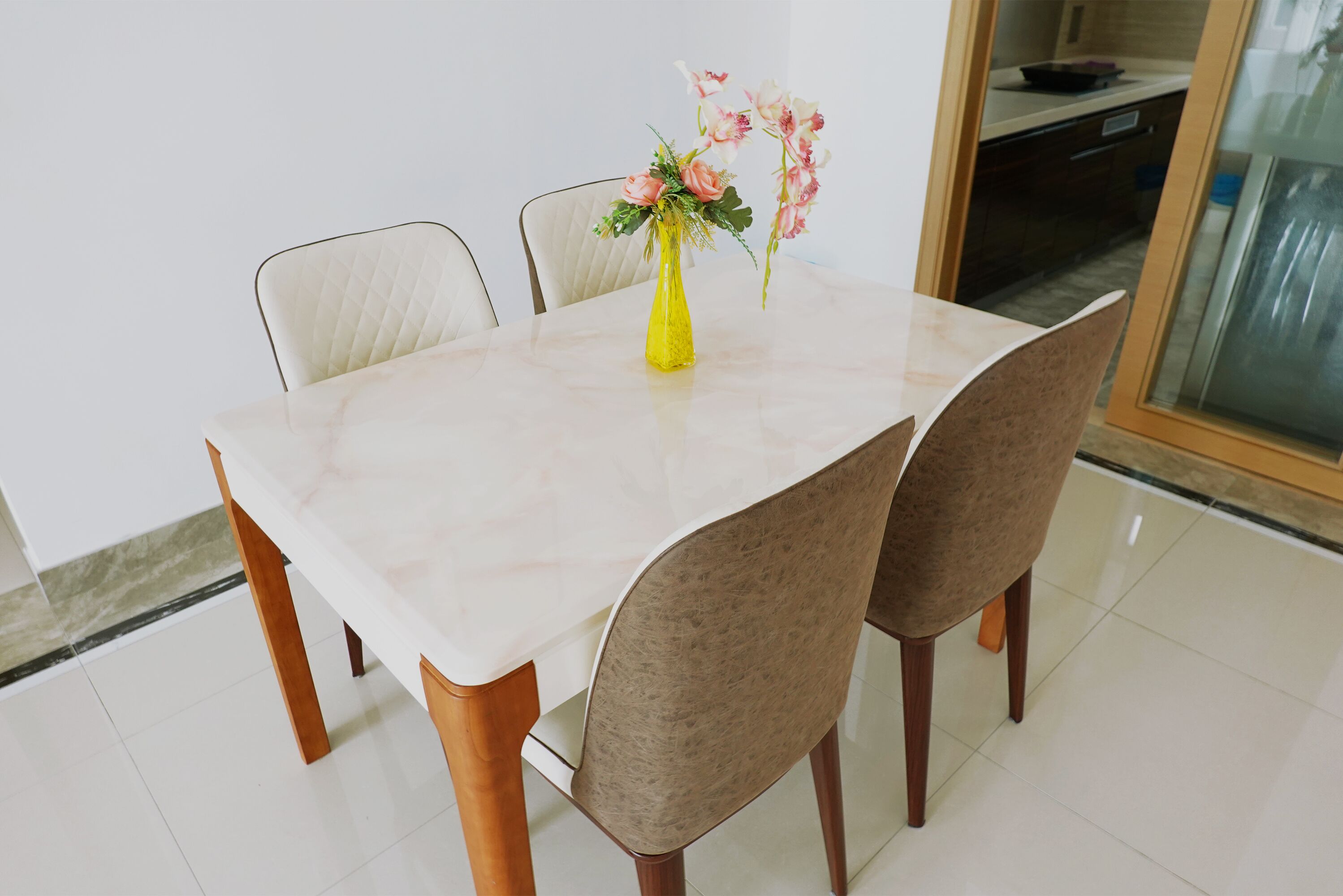 A dining table with a vase of flowers, two chairs, and a kitchen in the background.