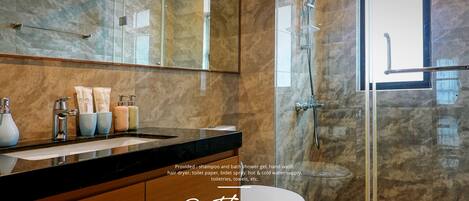 A modern bathroom with a glass shower enclosure, marble walls, and a vanity with toiletries.