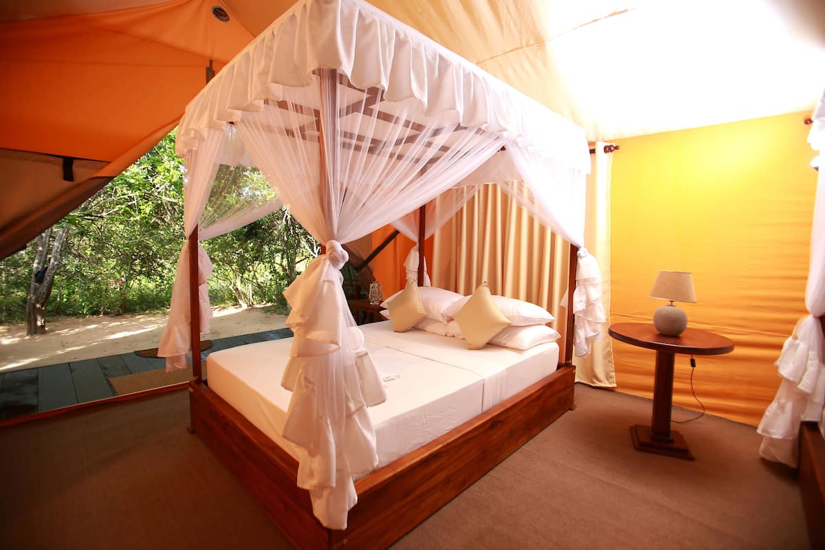 Une chambre aménagée comme une tente, avec un lit à baldaquin, une table de chevet avec une lampe et une vue sur la verdure environnante.