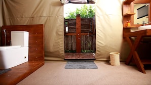 Una habitación con tienda, una cama de madera, una mesita de noche blanca, una alfombra pequeña, una cesta de mimbre y un mueble de madera con espejo.