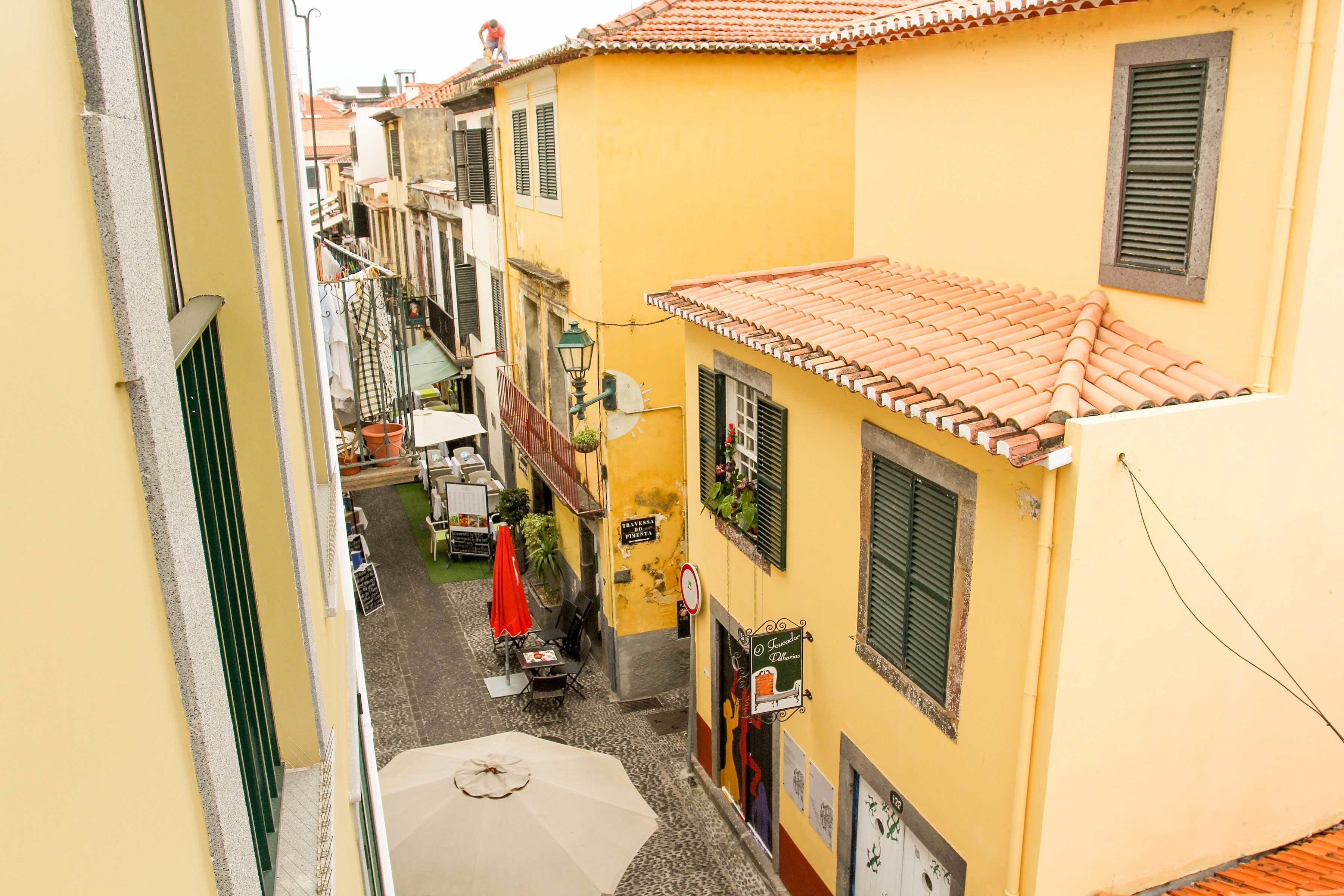 A narrow street with yellow buildings, a red umbrella, and a sign for a restaurant.